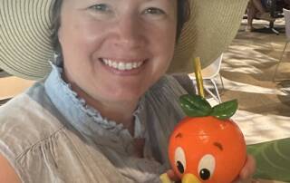 A selfie of Katie in a hat holding a drink in a orange bird-themed cup.