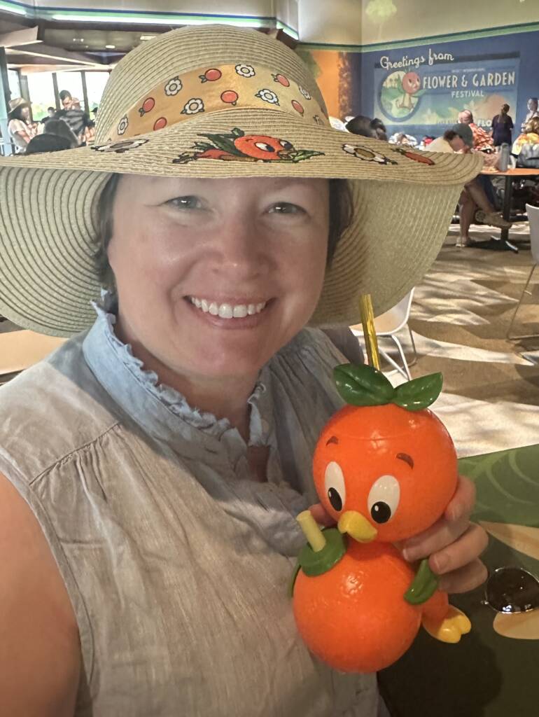 IMG_5373 A selfie of Katie in a hat holding a drink in a orange bird-themed cup.
