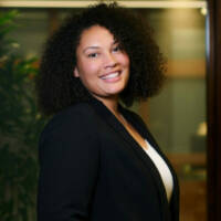 Cecily-Cliff Ceceily smiling, with curly dark brown hair, wearing a blazer