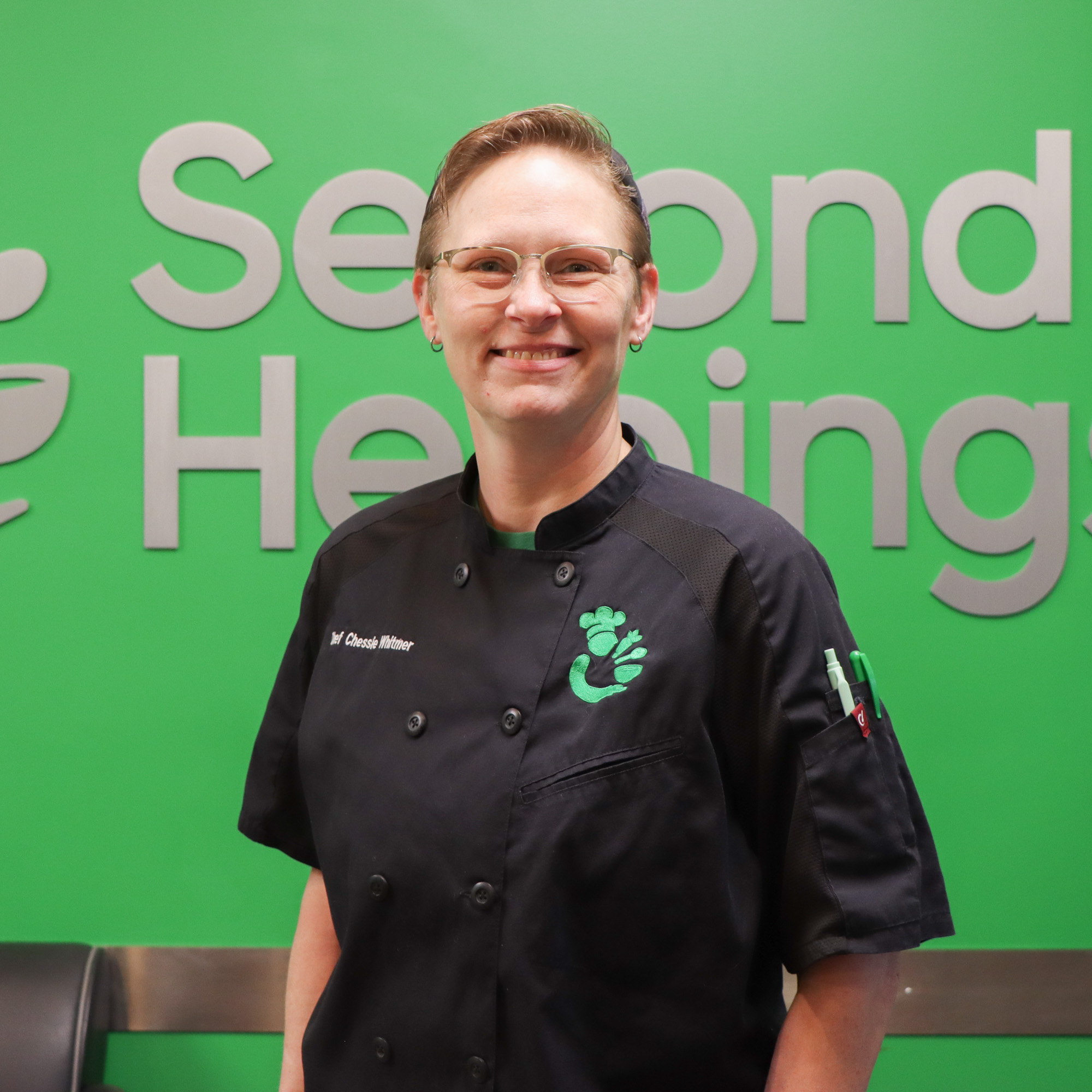 Chessie wearing a black chef coat and wire frame glasses