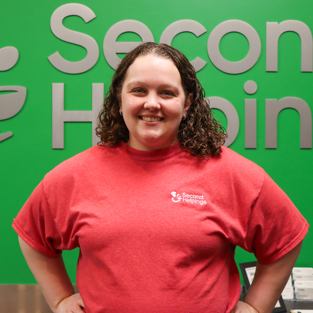 Nicole with brown curly hair wearing a red Second Helpings t-shirt