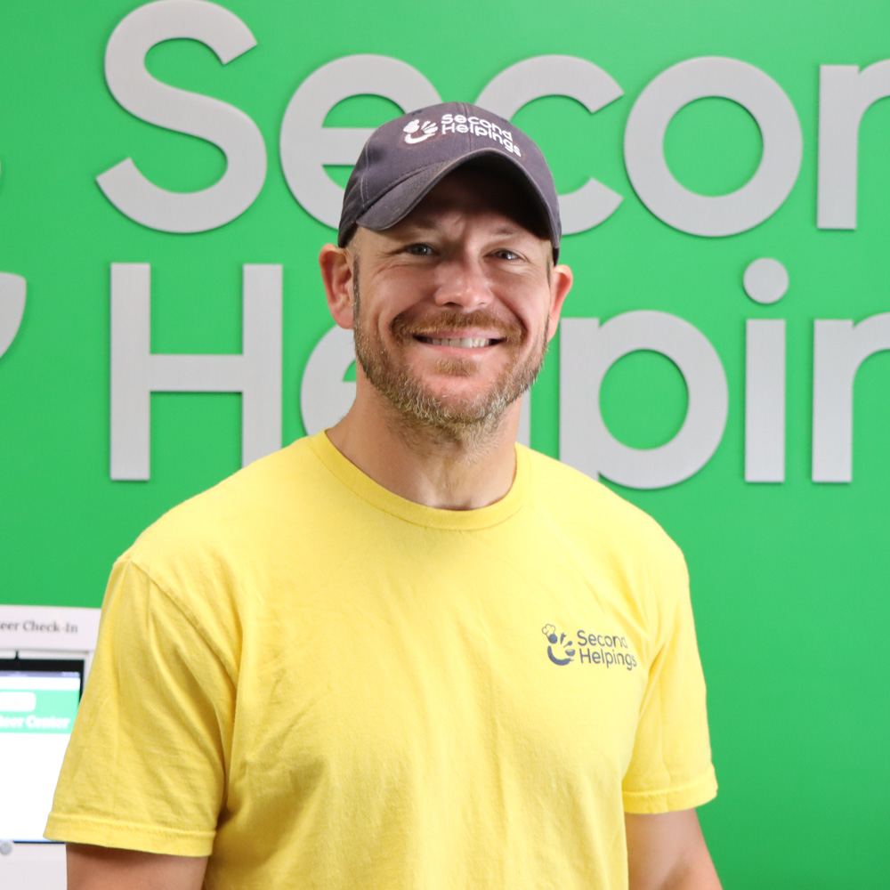 Evan Hefley Evan smiling, wearing a yellow Second Helpings shirt and blue Second Helpings cap